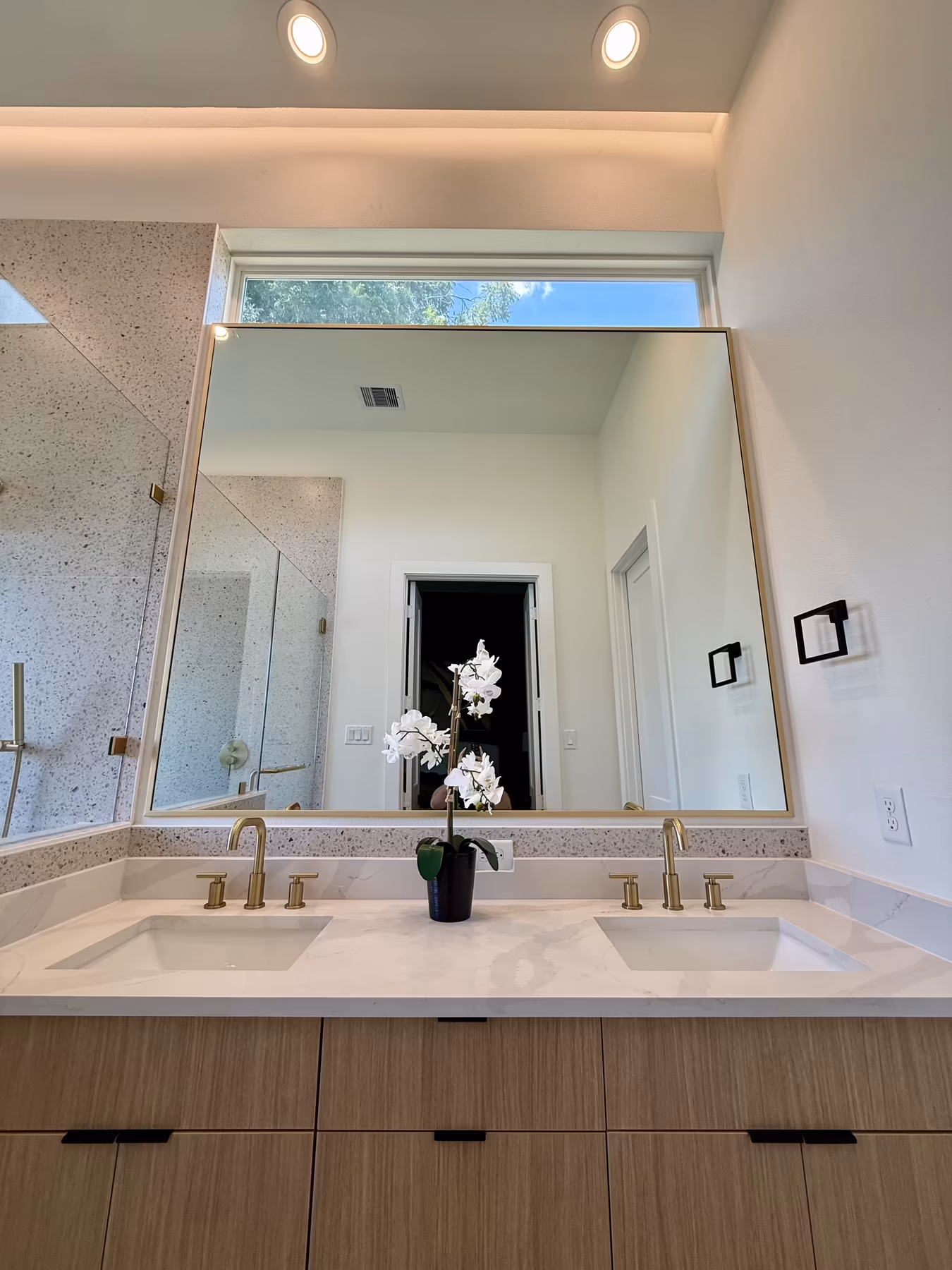 Large gold-framed double-vanity mirror beneath a clerestory window