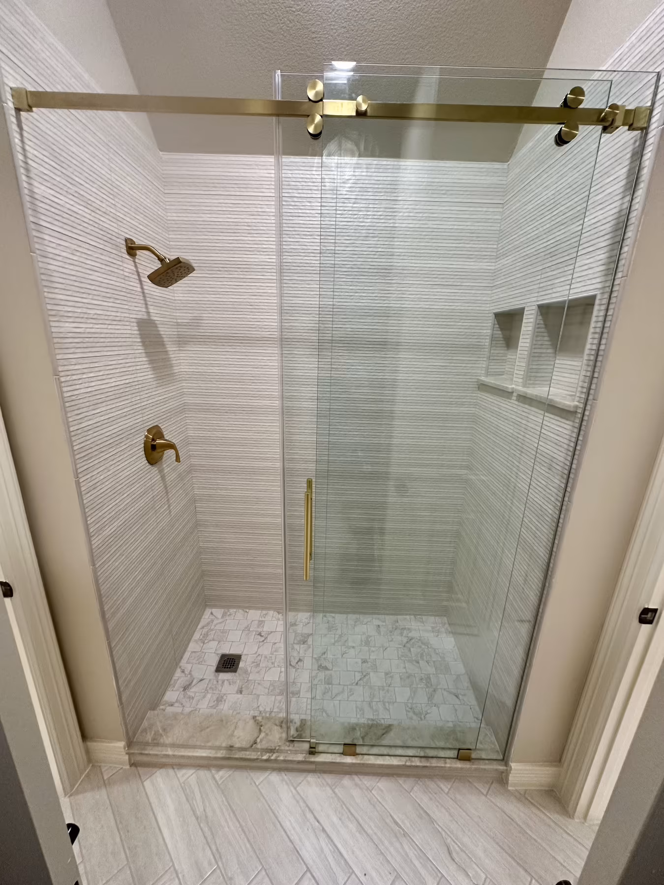 Frameless sliding shower enclosure with brushed-gold hardware and textured tile