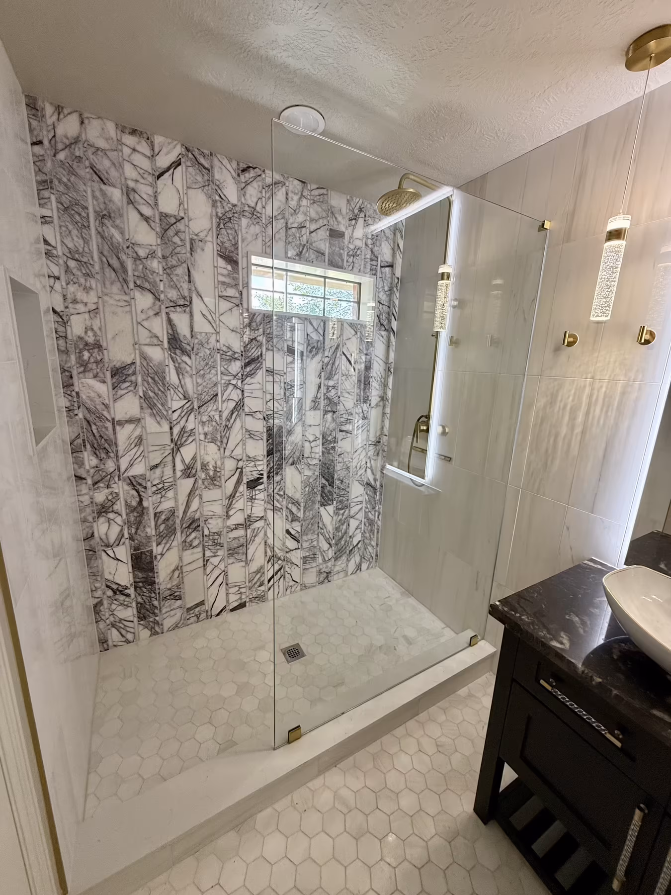 Frameless corner shower with dramatic book-matched marble feature wall and brushed-brass fixtures